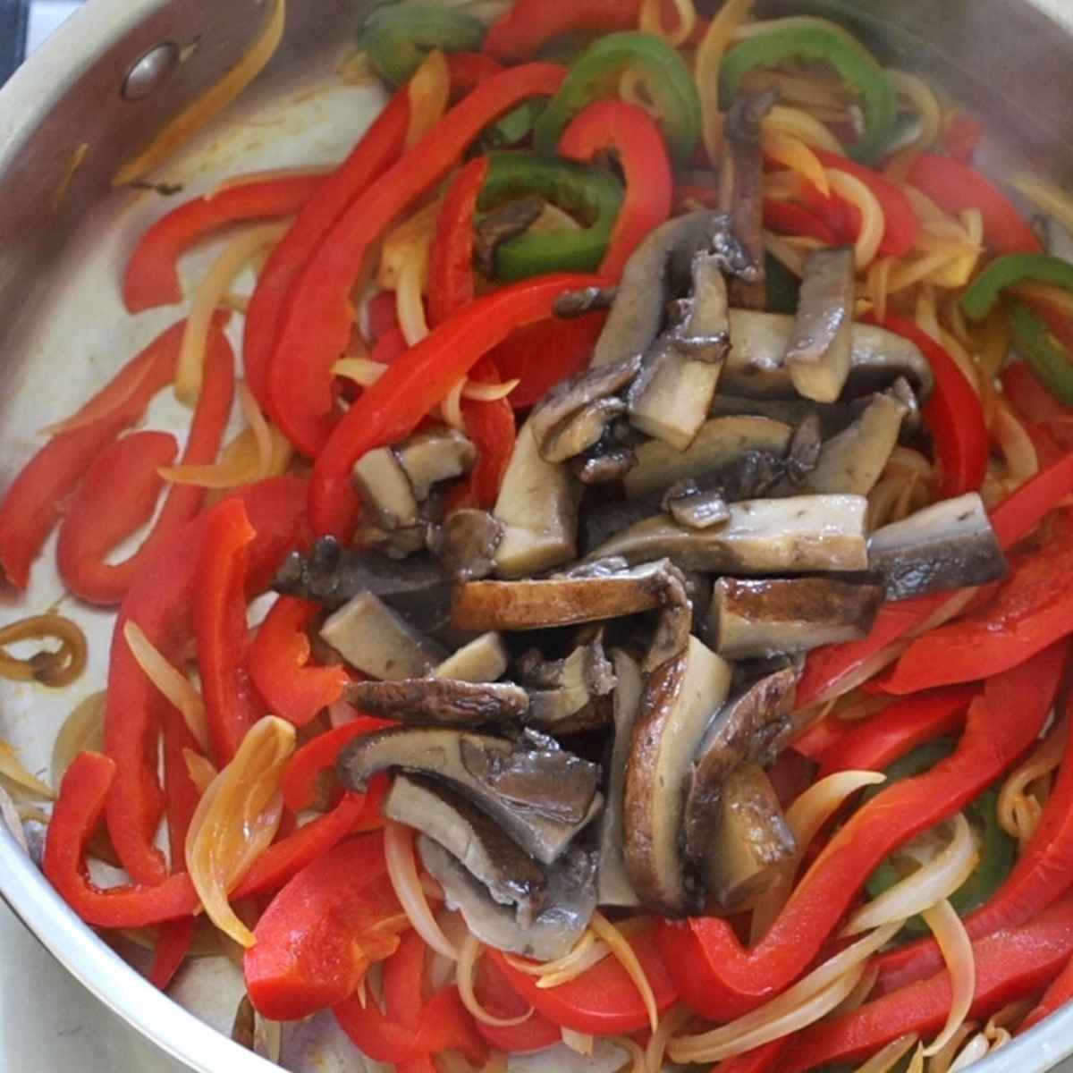 Red peppers, green jalapenos, brown portobello mushrooms all sliced and sauteed in a stainless steel skillet.