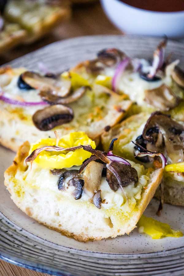A cheese and pepper hero made with french bread loaf cut in half and quartered then topped with oil, cheese, mushrooms, banana peppers, red onions, and black olives