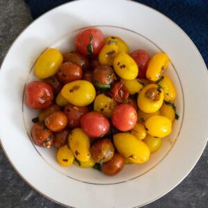 overhead view of red and yellow pan roasted grape tomatoes in a cream colored bowl with an inner and outer gold rim.