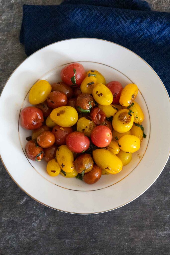 Overhead view of pan roasted tomatoes in a cream colored serving bowl with gold rings around the outer rim and inner circle of the bowl.